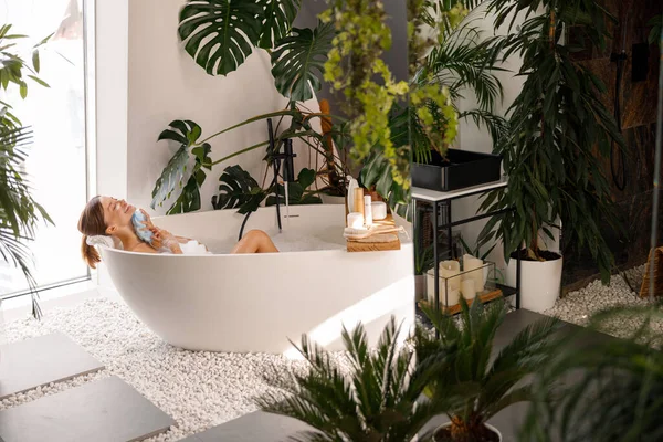 Entspannte junge Frau badet in modernem Badezimmer mit tropischen Pflanzen dekoriert — Stockfoto