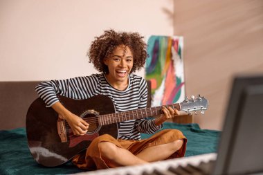 Evinde gitar çalan neşeli, çok kültürlü bir kadın.