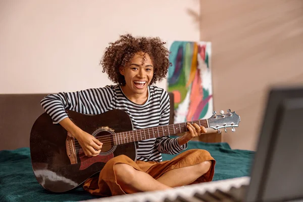Evinde gitar çalan neşeli, çok kültürlü bir kadın.