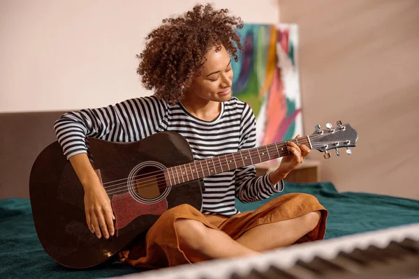 Багаторасова молода жінка грає на гітарі вдома — стокове фото