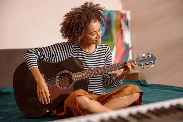Evde gitar çalan çok ırklı genç bir kadın.