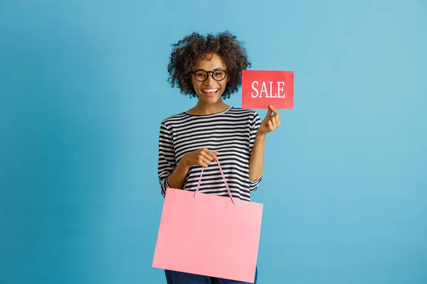 Cheerful woman holding purchases and sale card — Stockfoto