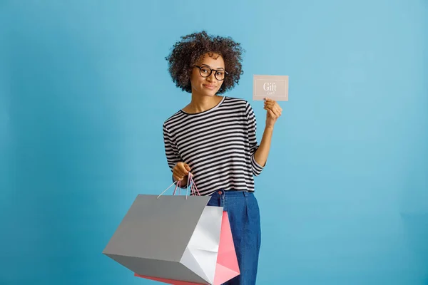 Joyful woman holding purchases and gift card — Stockfoto