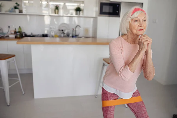 Senior vrouw stretching fitnessapparatuur in gezellige kamer — Stockfoto
