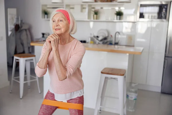 Oudere vrouw traint met weerstandsband binnen — Stockfoto