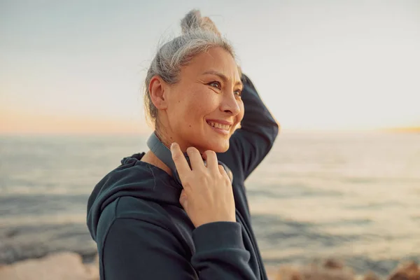 Encantadora deportista sosteniendo auriculares, de pie junto al mar —  Fotos de Stock