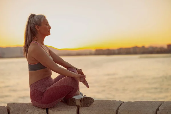 Frau in Sportkleidung meditiert in Lotusposition am Meer — Stockfoto