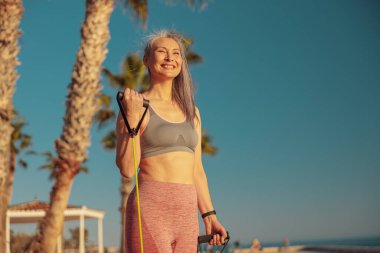 Spor tişörtlü ve taytlı kadın deniz kenarında spor yapıyor.