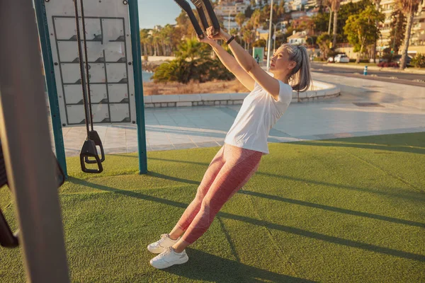 Foto de larga duración de la señora madura en ropa deportiva haciendo ejercicio en el campo de deportes al aire libre —  Fotos de Stock