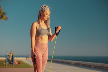 Toprağın yanında lastik bantlarla kollarını esneten odaklanmış bir kadın.