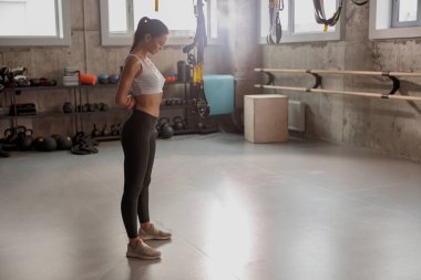 Genç, narin bayan ayakta dikiliyor ve spor salonuna bakıyor.