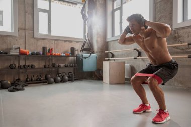 Zayıf, güçlü bir adam spor salonunda çömeliyor.