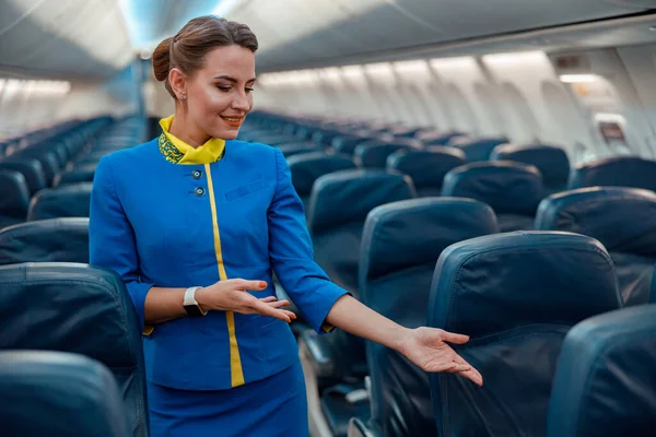 Mujer azafata señalando el asiento del pasajero en la cabina del avión — Foto de Stock