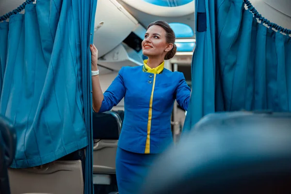 Mulher alegre aeromoça segurando cortinas em aviões de passageiros — Fotografia de Stock