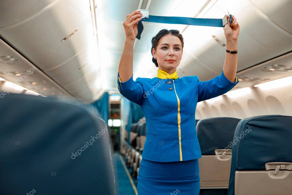 Female flight attendant with seatbelt standing in aircraft cabin
