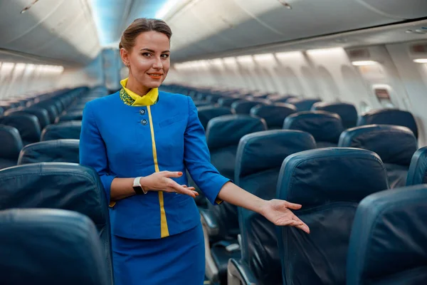 Female flight attendant pointing at passenger seat in airplane cabin — Stock Photo, Image