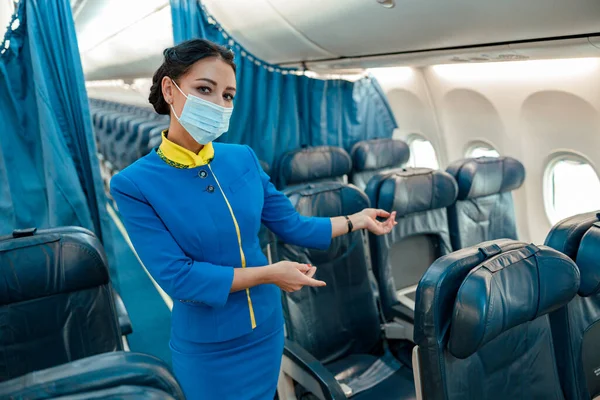 Letuška v lékařské masce zve na sedadlo spolujezdce v letadle — Stock fotografie