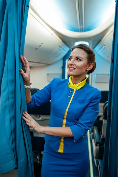 Allegro donna hostess aggiustare tende in aereo — Foto Stock