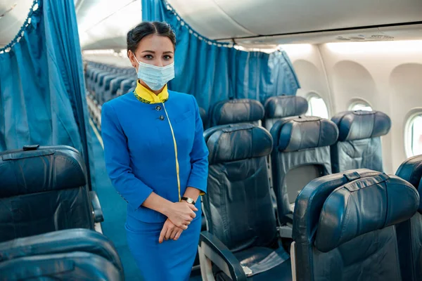 Letuška v lékařské masce stojící v kabině osobního letadla — Stock fotografie