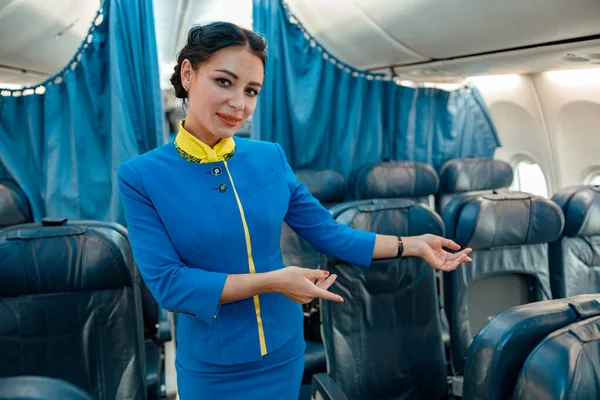 Žena letuška navrhuje sednout si na sedadlo spolujezdce v letadle — Stock fotografie