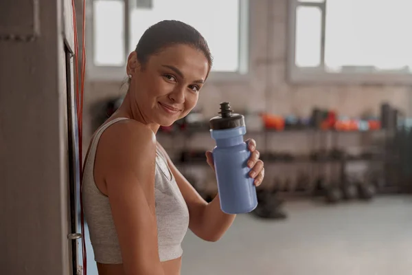 Mujer en ropa deportiva en el club deportivo, sonriendo y sosteniendo la botella de agua —  Fotos de Stock