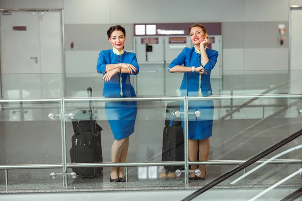 Dvě ženy letušky s cestovními taškami stojící na letišti terminálu — Stock fotografie