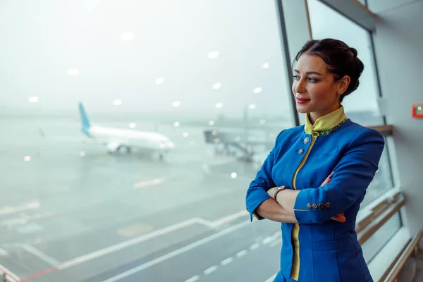 Kvinna flygvärdinna tittar ut genom fönstret i flygplatsterminalen — Stockfoto