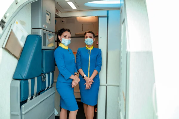 Letušky v lékařských maskách stojící v kabině letadla — Stock fotografie