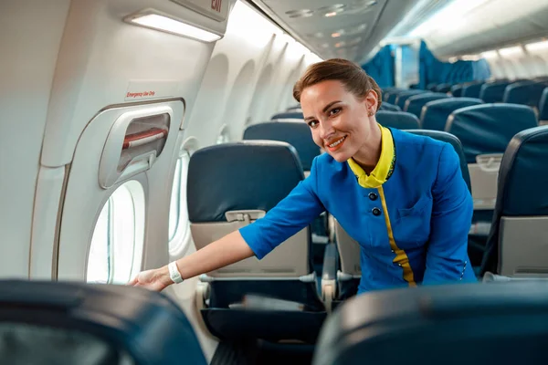 Χαρούμενη γυναίκα αεροσυνοδός στέκεται δίπλα στο παράθυρο στο αεροπλάνο — Φωτογραφία Αρχείου