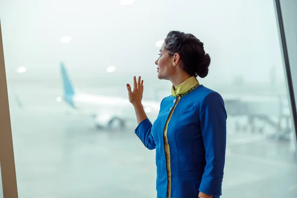 Woman stewardess placing hand on window in airport terminal — Stock Photo, Image