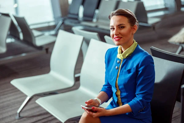 Joyful woman stewardess sitting on chair in airport departure lounge — Stock Photo, Image