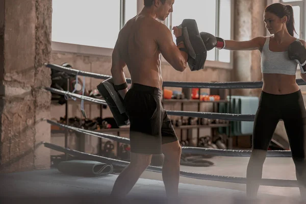 Kadın boksör boks kulübünde erkek antrenörle antrenman yapıyor.