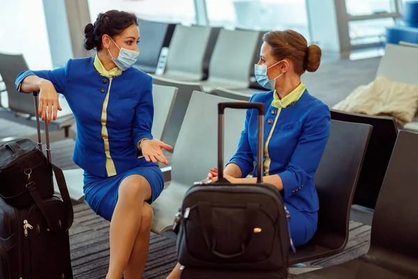 Assistenti di volo in maschere mediche seduti su sedie in aeroporto — Foto Stock