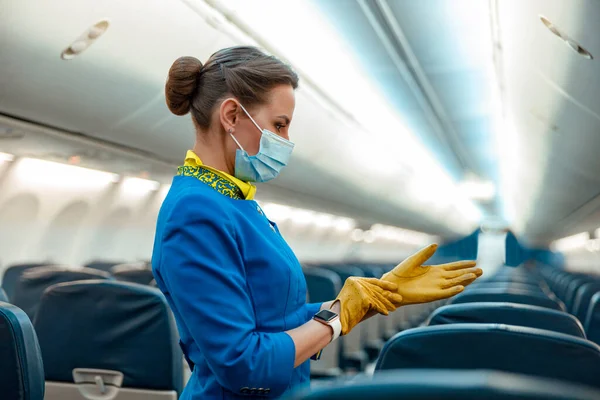 Letuška v lékařské masce nasazující si rukavice v letadle — Stock fotografie