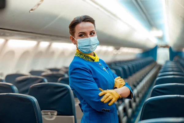 Letuška v lékařské masce stojící v leteckém salónu — Stock fotografie