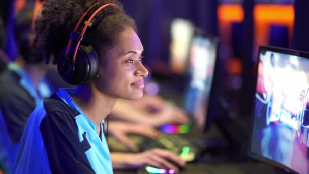 Młoda kobieta ze słuchawkami grająca w grę komputerową w klubie internetowym — Wideo stockowe
