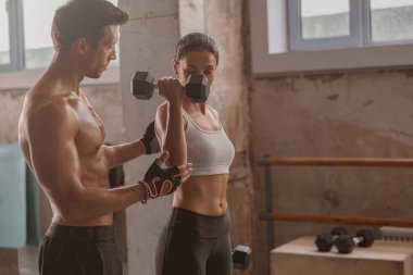 Spor salonunda atletik bir kadınla spor yapan kaslı bir adam.