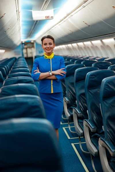 Alegre azafata mujer de pie en cabina de pasajeros de avión —  Fotos de Stock