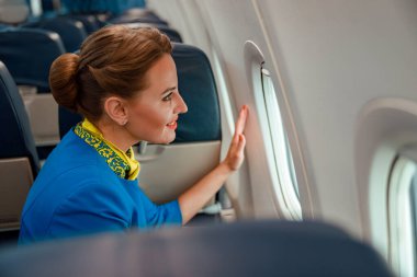Neşeli kadın hostes uçağın camından dışarı bakıyor.
