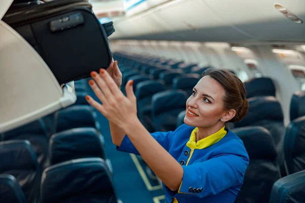 Azafata de aire poniendo bolsa de viaje en la papelera de equipaje en el avión —  Fotos de Stock