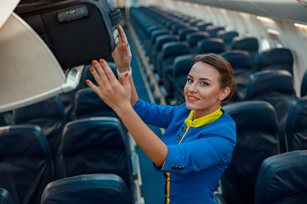 Azafata poniendo bolsa de viaje en la estantería de equipaje en el avión —  Fotos de Stock