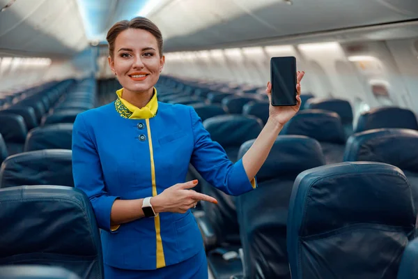 Gioiosa hostess con smartphone in piedi in cabina d'aereo — Foto Stock