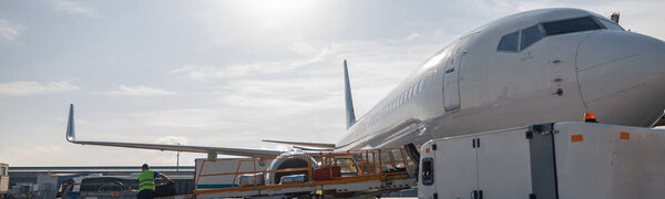 Worker loading baggage on conveyor belt to an airplane outdoors on a daytime