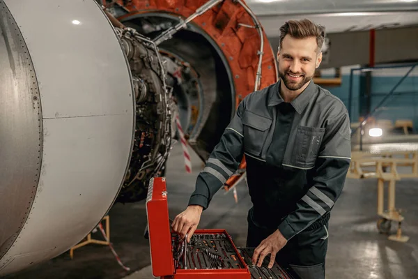 Hangarda alet çantası kullanan neşeli bir uçak tamircisi.
