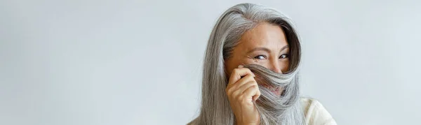 Positif moyen âge asiatique dame utilise les cheveux blancs comme niqab assis sur chaise en studio — Photo