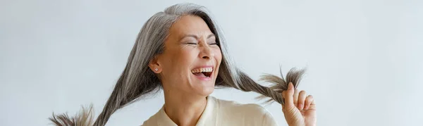 Ásia senhora segura longo hoary cabelo rindo no luz cinza fundo — Fotografia de Stock