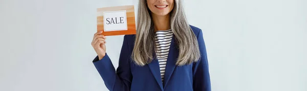 Hübsche asiatische Dame mit grauen Haaren hält Karte mit Wort Verkauf auf hellem Hintergrund — Stockfoto