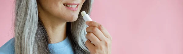 Frau mittleren Alters trägt Lippenbalsam auf rosa Hintergrund im Studio auf — Stockfoto