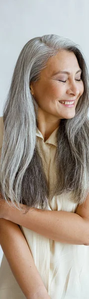 Shying mujer asiática de mediana edad con el pelo largo y plateado posa sobre fondo gris claro —  Fotos de Stock
