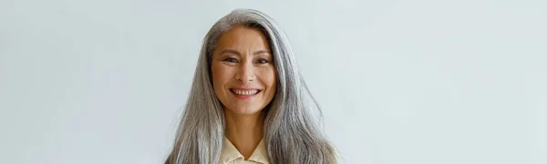 Portret van glimlachende Aziatische vrouw met roodharig haar en gekruiste armen op grijze achtergrond — Stockfoto